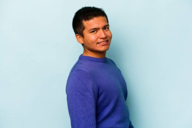 Latin kökenli genç adam mavi arka planda izole edilmiş. Kendine güveniyor. Kalçaları tutuyor..