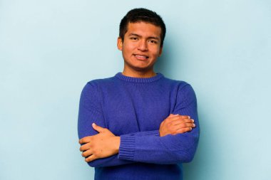 Mavi arka planda kendini güvende hisseden, kararlılıkla kollarını kavuşturan genç İspanyol bir adam..
