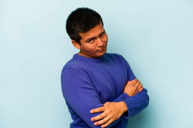 Genç İspanyol bir adam mavi arka planda izole edilmiş şüpheli, belirsiz, seni muayene ediyor..