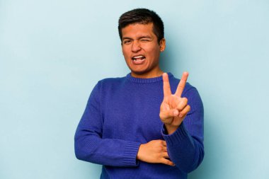 Mavi arka planda izole edilmiş genç İspanyol adam iki numarayı parmaklarıyla gösteriyor..