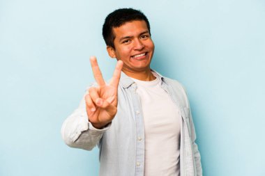 Mavi arka planda izole edilmiş genç İspanyol adam neşeli ve kaygısız parmakları olan bir barış sembolü gösteriyor..