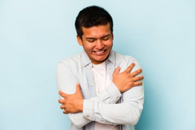 Genç İspanyol adam mavi arka planda izole edilmiş gülüyor ve eğleniyor..