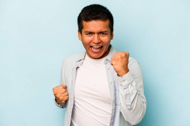 Genç İspanyol adam mavi arka planda izole edilmiş kaygısız ve heyecanlı tezahüratlar yapıyor. Zafer konsepti.