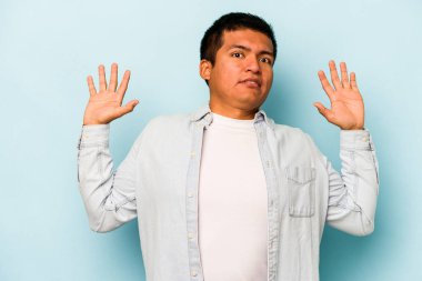 Genç İspanyol bir adam mavi arka planda izole edilmiş. Yakın bir tehlike nedeniyle şok oluyor.