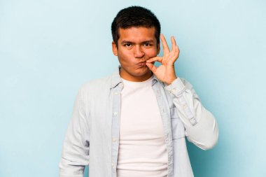 Genç İspanyol adam mavi arka planda izole edilmiş, parmakları dudaklarında bir sır saklıyor..