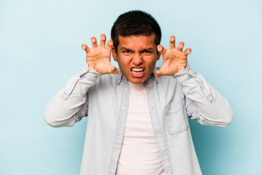 Mavi arka planda izole edilmiş genç İspanyol bir adam pençelerini bir kediyi taklit ederken gösteriyor, agresif bir hareket..