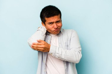 Genç İspanyol bir adam mavi arka planda izole edilmiş. Stres yüzünden boynu ağrıyor. Masaj yapıyor ve elle dokunuyor..