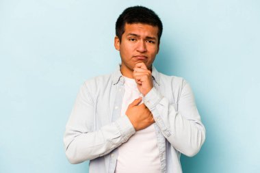 Genç İspanyol adam mavi arka planda izole edilmiş düşünüyor, bakıyor, yansıtıyor, düşünüyor, hayal kuruyor..