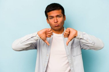 Genç İspanyol bir adam mavi arka planda izole edilmiş. Hoşlanmadığı bir hareket gösteriyor. Anlaşmazlık konsepti.