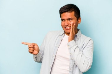 Genç İspanyol bir adam mavi arka planda izole edilmiş. Dedikodu yapıyor, bir şeyleri bildiriyor..