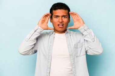 Genç İspanyol bir adam mavi arka planda izole edilmiş. Hoş bir sürpriz bekliyor. Heyecanlı ve el kaldırıyor..