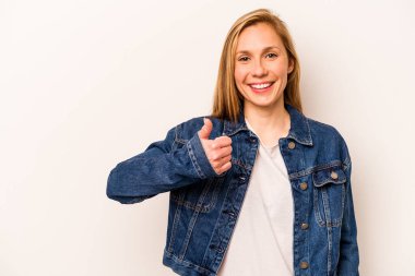 Beyaz arka planda izole edilmiş genç beyaz kadın gülümsüyor ve başparmağını kaldırıyor.