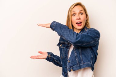 Beyaz arka planda izole genç beyaz kadın şok ve hayret içinde elleri arasında bir kopya alanı tutuyor.