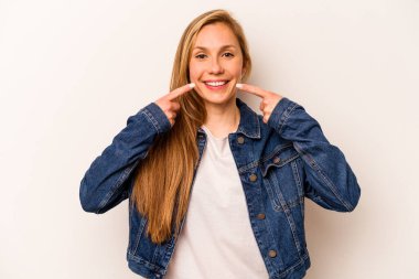 Beyaz arka planda izole edilmiş genç beyaz kadın gülümsüyor, parmaklarını ağıza doğrultuyor..