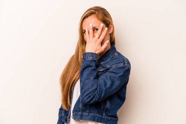 Beyaz arka planda izole edilmiş genç beyaz kadın kameraya parmaklarıyla göz kırpıyor, yüzünü kapatmaktan utanıyor..