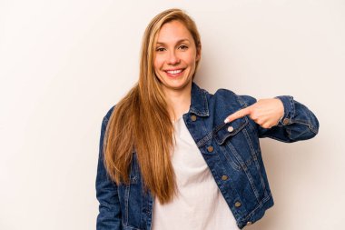 Beyaz arka planda yaşayan beyaz tenli genç bir kadın gömlek fotokopi alanını elle işaret ediyor, gururlu ve kendinden emin