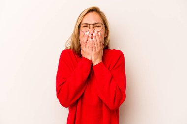 Beyaz arka planda izole edilmiş genç beyaz bir kadın bir şeye gülüyor, elleriyle ağzını kapatıyor..