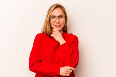 Beyaz arka planda izole edilmiş genç beyaz kadın mutlu ve kendinden emin gülümsüyor, elleriyle çenesine dokunuyor..