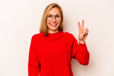 Beyaz arka planda izole edilmiş genç beyaz kadın neşeli ve kaygısız parmakları olan bir barış sembolü gösteriyor..