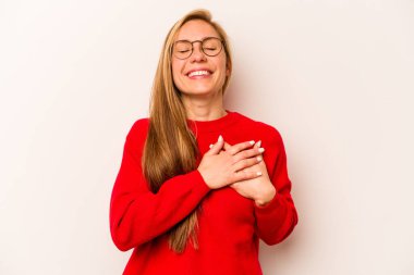 Beyaz arka planda soyutlanmış beyaz tenli genç bir kadın gülüyor, ellerini kalbe koyuyor, mutluluk kavramını koruyor..