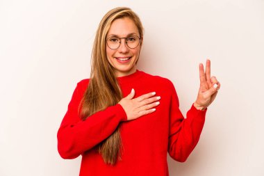 Beyaz arka planda izole edilmiş genç beyaz kadın yemin ediyor, elini göğsüne koyuyor..