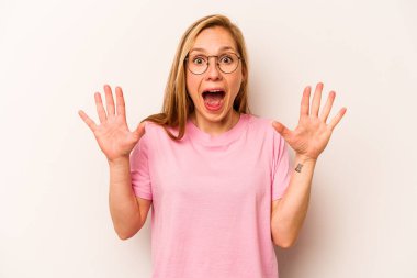 Beyaz arka planda izole genç beyaz kadın hoş bir sürpriz alıyor, heyecanlı ve el kaldırıyor..