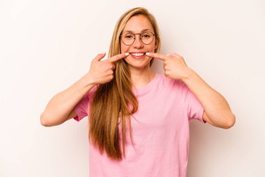 Beyaz arka planda izole edilmiş genç beyaz kadın gülümsüyor, parmaklarını ağıza doğrultuyor..