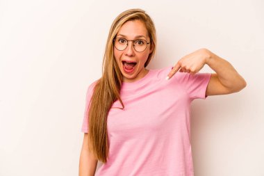Beyaz arka planda yaşayan beyaz tenli genç bir kadın gömlek fotokopi alanını elle işaret ediyor, gururlu ve kendinden emin
