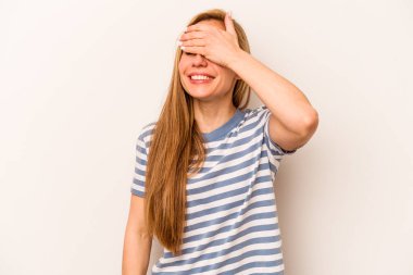 Beyaz arka planda soyutlanmış beyaz tenli genç bir kadın elleriyle gözlerini kapatıyor, geniş bir gülümsemeyle bir sürpriz bekliyor..