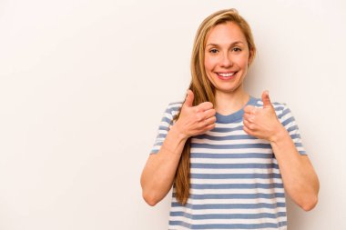 Beyaz arka planda izole edilmiş genç beyaz kadın gülümsüyor ve başparmağını kaldırıyor.