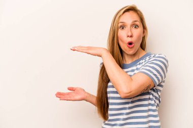 Beyaz arka planda izole genç beyaz kadın şok ve hayret içinde elleri arasında bir kopya alanı tutuyor.