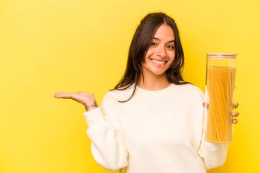 Sarı arka planda izole edilmiş spagetti kavanozunu tutan genç İspanyol kadın bir avuç içinde fotokopi alanı ve belinde bir el daha olduğunu gösteriyor..