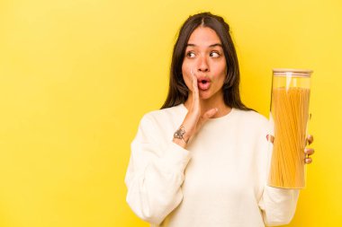Sarı arka planda izole edilmiş spagetti kavanozunu tutan genç İspanyol kadın gizli bir sıcak fren haberi veriyor ve yan bakıyor.