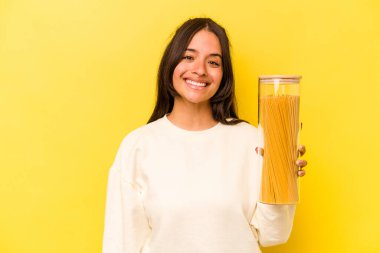 Sarı arka planda izole edilmiş spagetti kavanozunu tutan genç İspanyol kadın mutlu, gülümseyen ve neşeli..