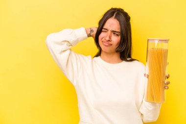 Sarı arka planda izole edilmiş spagetti kavanozunu tutan genç İspanyol kadın kafasının arkasına dokunuyor, düşünüyor ve bir seçim yapıyor..