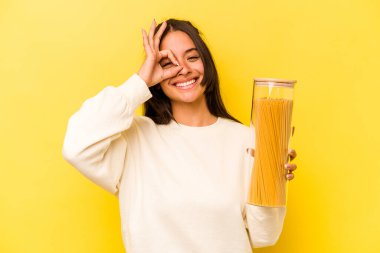 Sarı arka planda izole edilmiş spagetti kavanozu tutan genç İspanyol kadın..