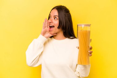 Sarı arka planda izole edilmiş spagetti kavanozunu tutan genç İspanyol kadın bağırıyor ve avuç içini açık tutuyor..