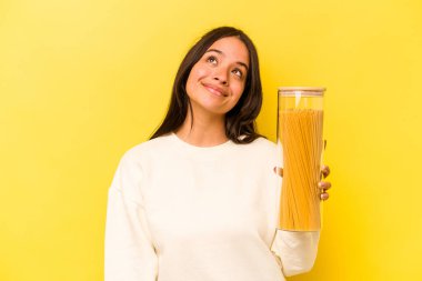 Genç İspanyol kadın elinde spagetti kavanozuyla sarı arka planda izole bir şekilde amaçlarına ve amaçlarına ulaşmayı hayal ediyor.