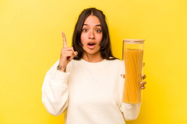 Sarı arka planda izole edilmiş spagetti kavanozunu tutan genç İspanyol kadının bir fikri var, ilham verici bir kavram..
