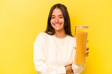 Sarı arka planda izole edilmiş spagetti kavanozunu tutan genç İspanyol kadın gülüyor ve eğleniyor..
