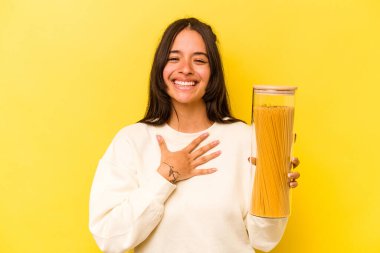 Sarı arka planda izole edilmiş spagetti kavanozunu tutan genç İspanyol kadın kahkahalar atıyor..