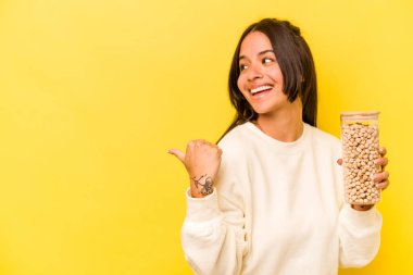 Genç İspanyol kadın elinde nohut kavanozuyla sarı arka planda izole edilmiş, baş parmak uzakta, gülen ve kaygısız..