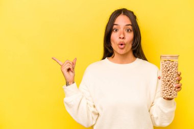 Sarı arka planda izole edilmiş nohut kavanozu tutan genç İspanyol kadın...
