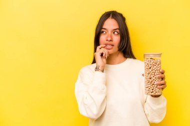 Sarı arka planda izole edilmiş nohut kavanozunu tutan genç İspanyol kadın bir şeyin fotokopi odasına baktığını düşünerek rahatladı..