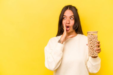 Sarı arka planda izole edilmiş nohut kavanozunu tutan genç İspanyol kadın gizli bir sıcak fren haberi veriyor ve yan bakıyor.