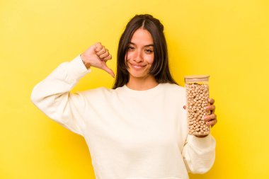 Sarı arka planda izole edilmiş nohut kavanozunu tutan genç İspanyol kadın gururlu ve kendinden emin hissediyor, örnek olarak..