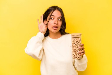 Sarı arka planda izole edilmiş nohut kavanozunu tutan genç İspanyol kadın bir dedikoduyu dinlemeye çalışıyor..