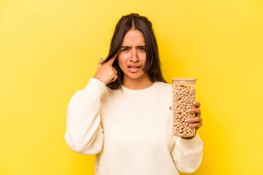 Sarı arka planda izole edilmiş nohut kavanozunu tutan genç İspanyol kadın işaret parmağıyla yaptığı hayal kırıklığını gösteriyor..