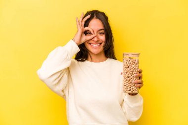 Sarı arka planda izole edilmiş nohut kavanozu tutan genç İspanyol kadın heyecanlı..