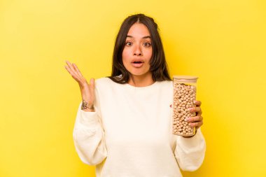 Elinde nohut kavanozu tutan genç İspanyol kadın sarı arka planda izole edilmiş şaşırmış ve şok olmuştu..